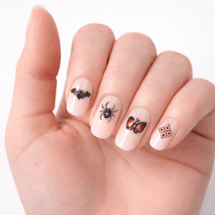 En hånd med lys neglelakk har neglelakk med Halloween-tema: en svart flaggermus, en svart edderkopp, en rød og svart marihøne og et hvitt firkantet motiv på ulike fingernegler.