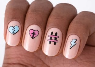 En hand med fyra naglar målade med olika mönster: ett blått krossat hjärta, ett rosa hjärta med ett svart kors, en rosa och svart hashtag-symbol och en vit blixt på en naken bas.
